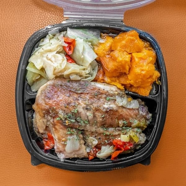 Soul food meal with baked chicken, cabbage, and candied yams in a black to-go container.