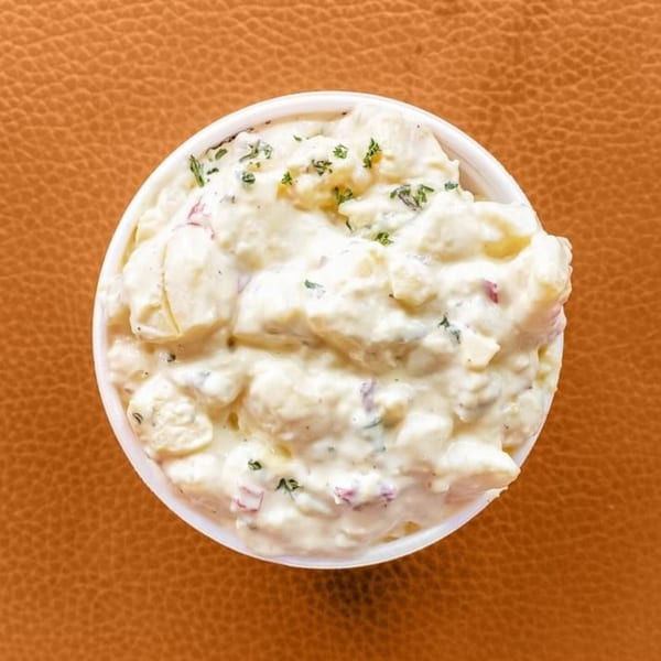 Creamy potato salad with herbs in a white bowl, a classic soul food side dish.