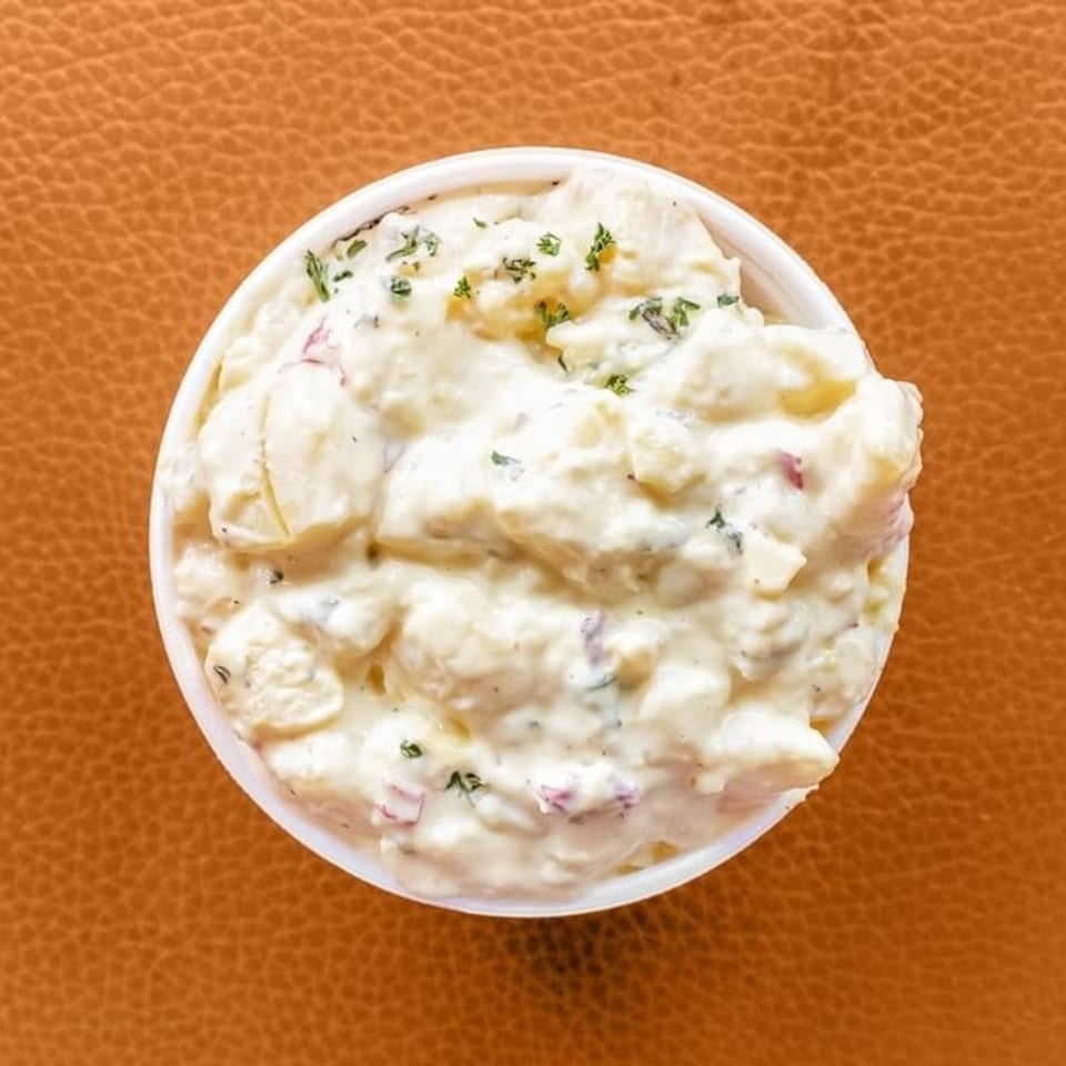 Creamy potato salad with herbs in a white bowl, a classic soul food side dish.