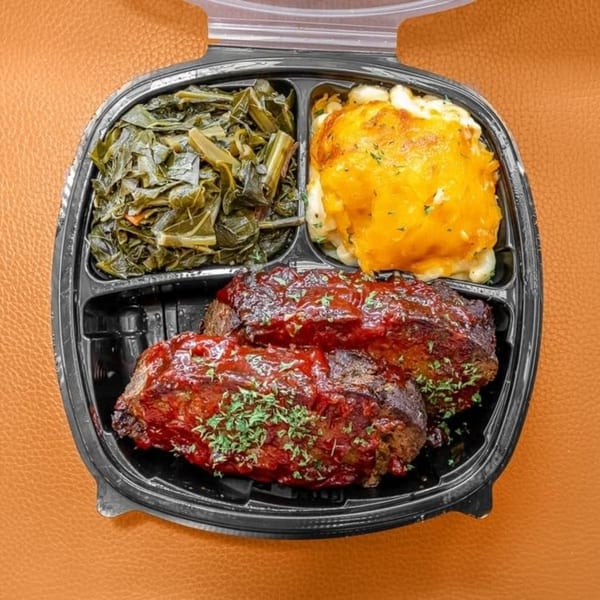 Ms. Ruby's soul food meal with meatloaf, collard greens, and macaroni and cheese in a to-go container.