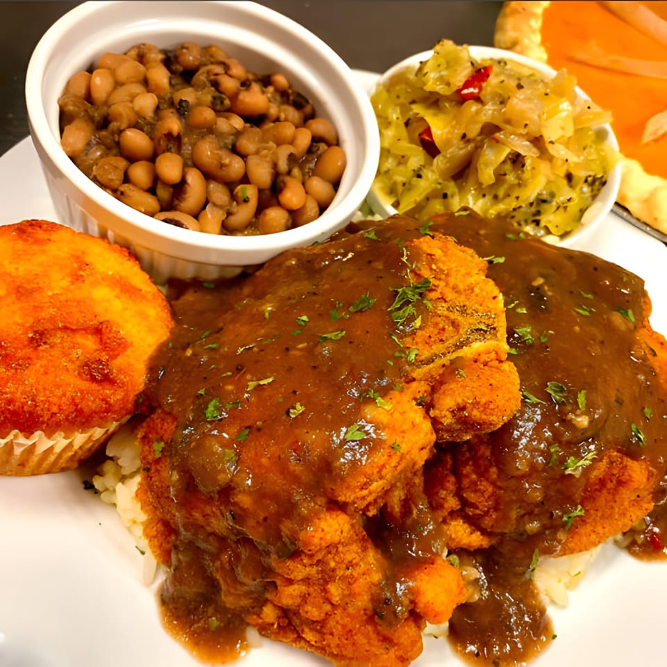Fried chicken with gravy, black-eyed peas, cabbage, and cornbread muffin on a white plate.