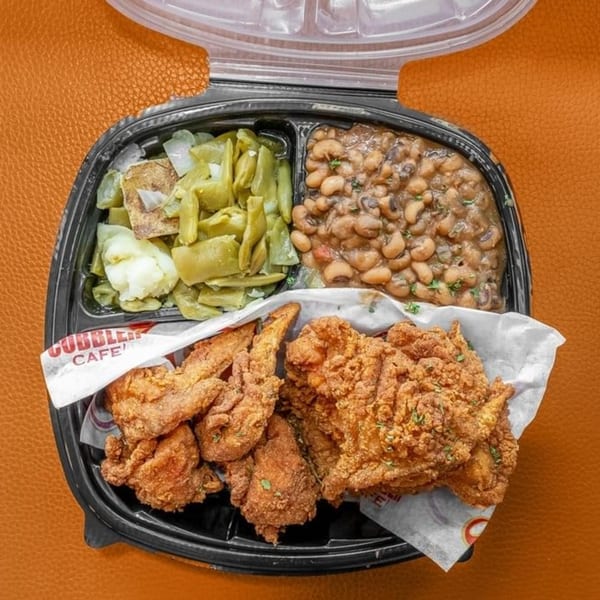 A soul food meal with fried chicken, green beans, and black-eyed peas in a to-go container.
